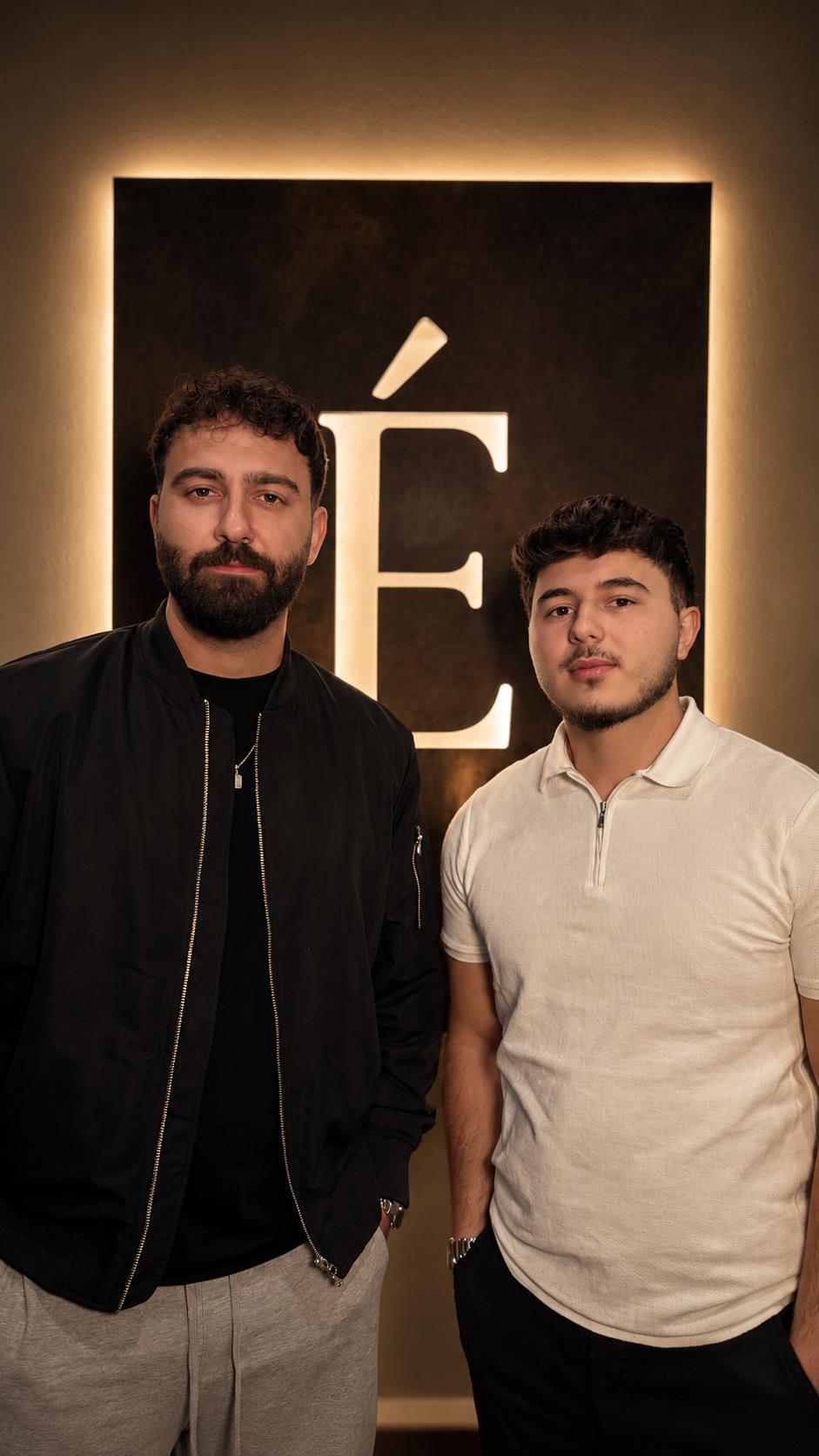 Hasan Aydin, BA (links) und Emircan Caliskan (rechts) vor dem beleuchteten É bei Élysée